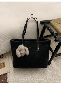 Detail of black suede tote bag with thin straps and a plush grey rabbit charm accessory