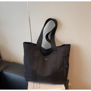 Detail of minimalist black nylon tote bag featuring a round metal logo and woven side tag
