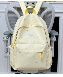 Detail of light yellow backpack with colorful polka dots and moon patterns on a chair