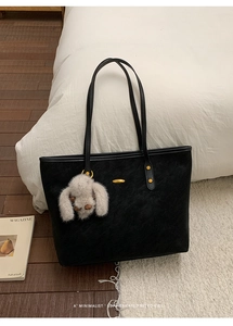 Detail view of a black suede tote bag featuring a cute long-eared rabbit plush charm
