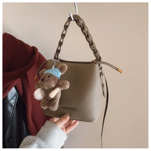 Detail of coffee brown pebble leather bucket bag with braided handle and bear charm