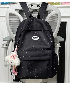 Close-up of black backpack with star patterns and plush dog charm on white chair