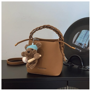 Detail of brown litchi leather bucket bag with woven handle and plush bear charm