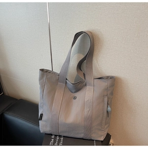 Detail of grey nylon tote bag showing side zipper pocket and branded logo tag