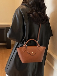 Retro brown lychee leather handbag with golden metal buckle worn over a black trench coat
