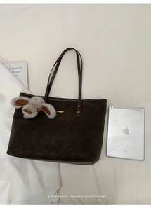 Flat lay of large dark brown suede tote bag with tablet and plush rabbit charm