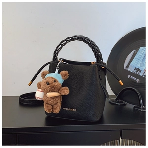 Detail of black pebbled leather bucket bag with braided handle and plush bear charm