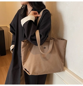 Detail view of the beige minimalist tote bag showing metal logo and dual handle straps