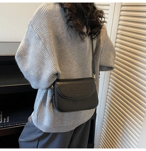 Detail of black leather crossbody bag with gold hardware worn over a grey sweater