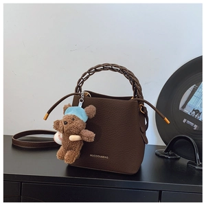 Close-up of deep coffee bucket bag with woven handle and plush bear pendant detail