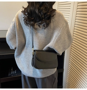 Detail of a minimalist black leather crossbody bag with gold hardware on a knit sweater