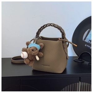 Detail of khaki bucket bag with lychee texture and cute plush bear accessory