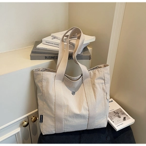 Detail of off-white canvas tote bag featuring reinforced straps and metallic logo