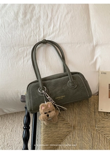 Detail of dark green leather shoulder bag with white stitching and plush dog charm