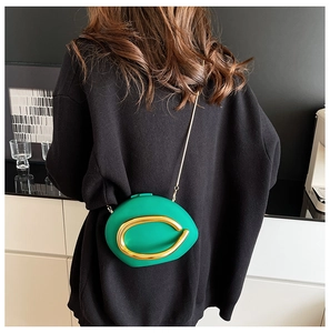 Detail view of a green asymmetrical crossbody bag with a large gold metal ring and chain
