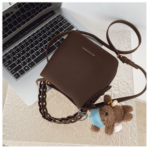 Detail of dark brown lychee texture bag with metal logo, chain strap, and bear charm