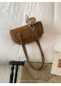 Detailed view of brown leather bag with gold lettering and cute plush bear accessory