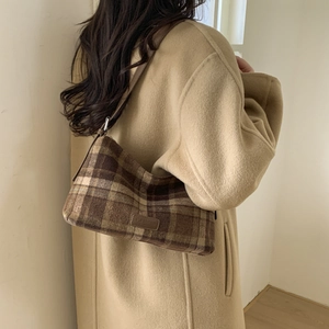 Sac baguette à carreaux marron avec écusson en cuir porté sur un manteau en laine beige chic