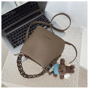 Detail of tan pebble leather bucket bag with chain handle and plush bear charm accent
