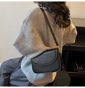 Detailed view of the sleek black leather shoulder bag worn by a model on a knit sweater