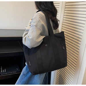 Close-up of a black casual tote bag with a circular metal logo and wide shoulder straps