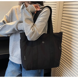 Detail of a large black tote bag with metal logo and fabric tag on casual model