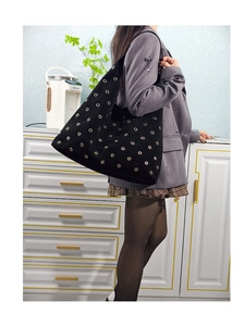 Detail view of a black suede tote bag with decorative gold eyelets worn on the shoulder