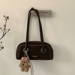 Detail of dark brown leather underarm bag with contrast stitching and teddy bear charm