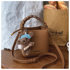 Brown litchi leather bucket bag featuring a woven handle and a cute plush bear charm