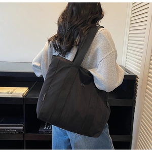 Detailed back view of a black large capacity canvas tote bag worn by a model in casual style
