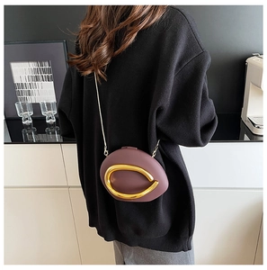 Detail of dark purple oval crossbody bag with large gold ring decoration and metal chain