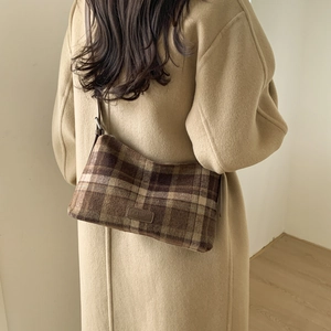 Détail du sac cabas à carreaux marron avec étiquette Fashion porté sur un manteau beige