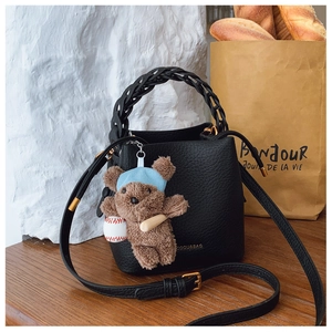 Detail of black lychee grain bucket bag with woven handle and brown plush bear charm