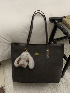 Large dark leather tote bag with elegant gold accents and a grey plush bunny pendant