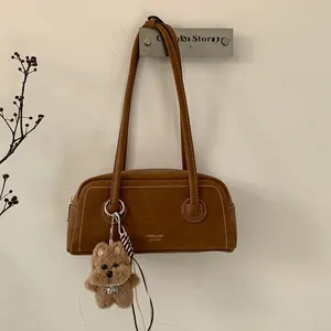 Close-up of brown leather underarm bag with white stitching and plush bear charm