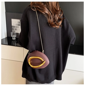 Detail of a dark reddish brown asymmetric crossbody bag with a gold circular metal accent