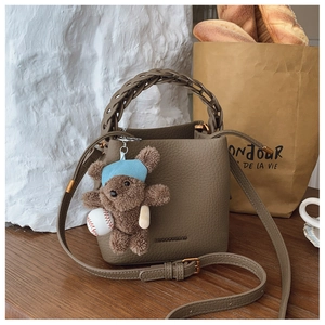 Close-up of brown pebbled leather bucket bag with woven handle and cute bear charm