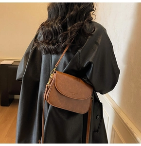 Close-up of a brown leather crossbody bag with adjustable strap and gold metal buckles