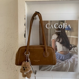 Detail of brown matte underarm bag with white logo and plush teddy bear charm accessory