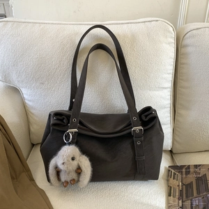 Detail of deep brown leather tote bag with plush rabbit charm on a soft white sofa