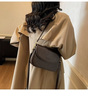 Detail of dark brown leather crossbody bag with metal buckle on a beige trench coat