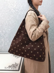 Brown suede tote bag with golden eyelets carried by a model in a beige trench coat