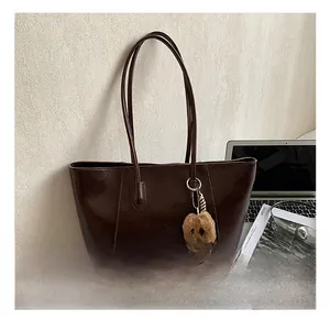 Macro view of dark brown vintage tote bag featuring a cute plush bear pendant and leather straps