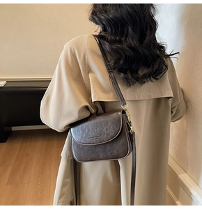 Detail of dark brown leather crossbody bag styled with a beige trench coat on a model