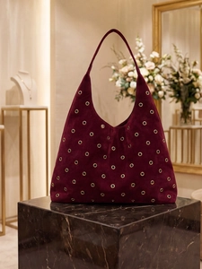 Elegant burgundy suede hobo bag with gold eyelet details on marble display