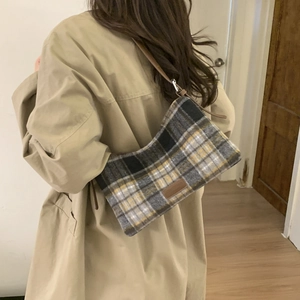 Détail du sac cabas vintage à carreaux avec écusson en cuir porté sur un trench-coat chic