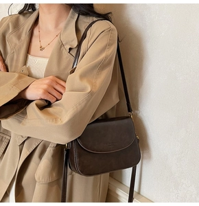 Detail of dark brown leather saddle bag with embossed logo and elegant flap design
