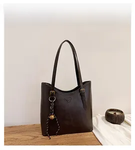 Detail view of a vintage dark brown tote bag with metal triangle plaque and bell charm