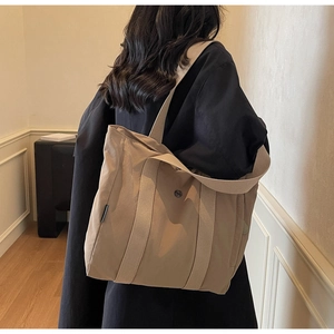 Detailed back view of a large khaki tote bag worn by a model in a minimalist room