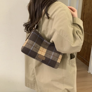 Détail de la texture en laine à carreaux vintage et logo en cuir sur un sac cabas